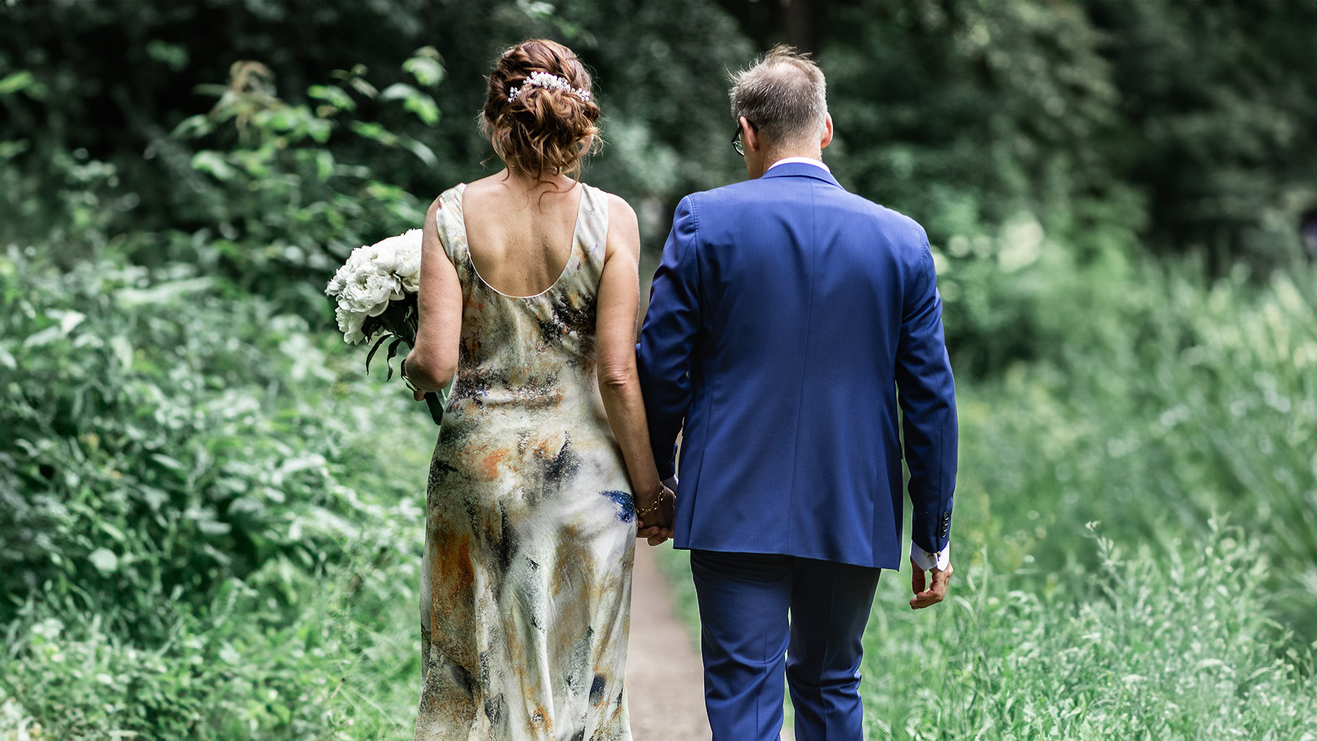 A bride and a groom walking away in nature.