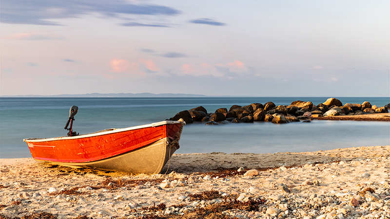 A boat on the beach in the sunset.